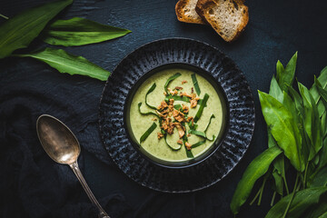 Wild garlic soup with wild garlic leaves and rosted onions on black background, top view