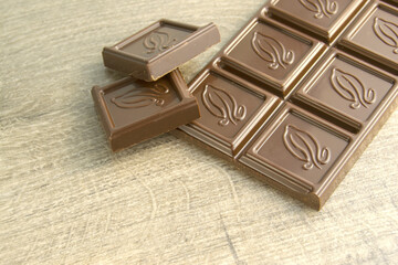bar of chocolate on a wooden background. pieces of chocolate lie next to the bar