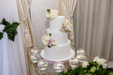 A large white wedding cake with figures of the bride and groom on a wooden stand in a restaurant. Cake for the bridal wedding ceremony.