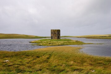 Fototapeta na wymiar Ruins of the Scolpaig Tower Georgian folly seen across Loch Scolpaig near the village of Scolpaig on the island of North Uist in the Outer Hebrides, Scotland, UK