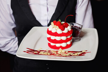 Delicious fresh millefeuille dessert on a white plate decorated with raspberries and cherry berries. Dessert on a large white plate in the hands of a waiter. Hands of a man without a face