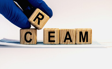 Text CREAM made from wooden cubes. Hands in a blue glove.