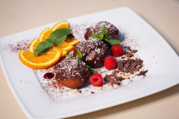 Three profiteroles covered with chocolate and coconut flakes decorated with orange and peanuts on a white plate