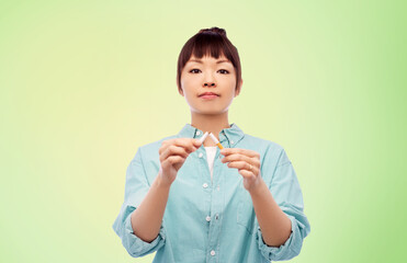 quit smoking and people concept - young asian woman braking cigarette over lime green natural background