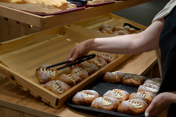 An employee of a bakery, self-service restaurant, lays out buns on a distribution line. Copispace.