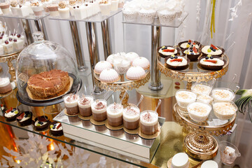 Wedding Candy Bar with a large three-story cake in a classic style. Table with sweets and desserts for guests at the holiday. White sweet desserts are not harmful to the figure. 