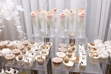 Wedding Candy Bar with a large three-story cake in a classic style. Table with sweets and desserts for guests at the holiday. White sweet desserts are not harmful to the figure. 