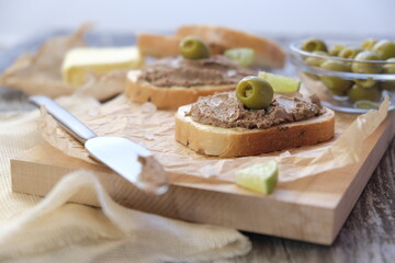 Breakfast: bread with chicken liver pate served with a slice of lime and green olive on wooden background.