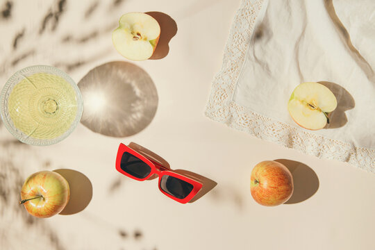 Summer still life composition made of apples, glass with juice and sunglases on pastel background white cloth. Creative layout. Freshness concept. Top view. Flat lay.