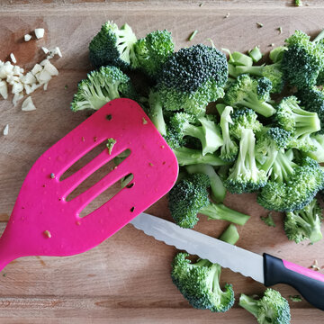 Broccoli in Stücke geschnitten auf Schneidebrett mit Knoblauch und Messer und Pfannenheber