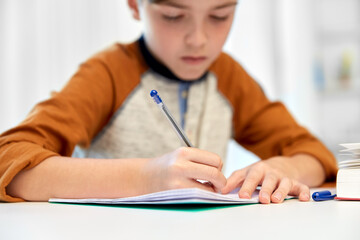 Fototapeta premium children, education and learning concept - student boy with book writing to notebook at home