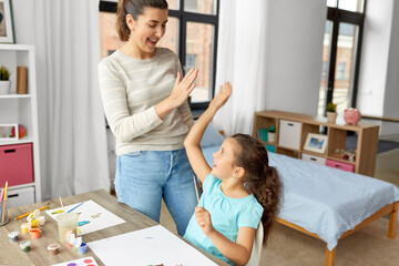 Fototapeta premium family, motherhood and leisure concept - mother spending time with her little daughter drawing with colors and making high five gesture at home