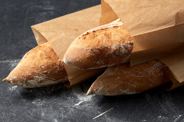 food, baking and cooking concept - close up of baguette bread in paper bags on table over dark...