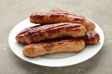 Grilled sausages on white plate on grey background