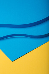 Abstract minimal paper background. Two blue curvy cut out paper stripes on blue and yellow paper background.