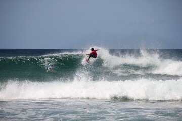 A young, sporty dark tanned male surfer in dynamic motion riding down the lip of a beautifully clear turquoise wave of medium size at Ocean Beach near Whangarei Heads, New Zealand