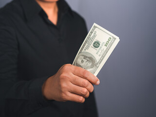 Businessman wearing a black shirt hand holding of US banknote while standing in a studio. Close-up photo. Business and finance concept