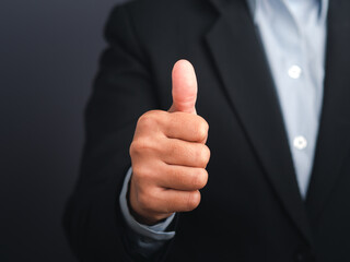 Businessman showing thumbs up like hand sign gesture against a gray color background. Happy confident man gesture. Space for text. Success in business