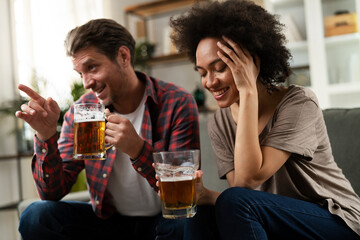 Boyfriend and girlfriend drinking beer at home. Happy couple watching sports game on tv..