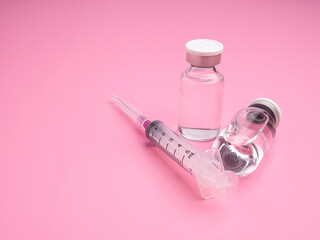 The vaccine in glass bottles with a syringe placed on a light pink background. Vaccine for immunization, and treatment from virus infection. Top view. Concept of medical and healthcar