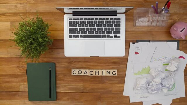 Term coaching is collected from wooden cubes with letters on the table, view from above. Word coaching is made by hands from a cube on a desktop in the office. Concept of training and teaching.