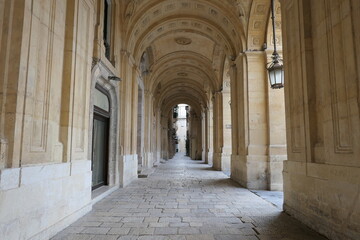 Valletta, Malta, March 17, 2021: Well worn limestone paving and ornate arches in the arcade at the front of the National Library of Malta.