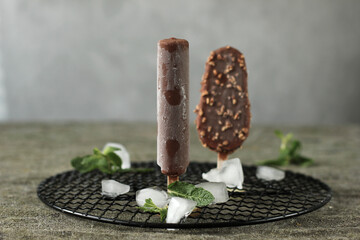 Close-up of  two chocolate-covered ice creams on black grid next to ice and mint with copy space