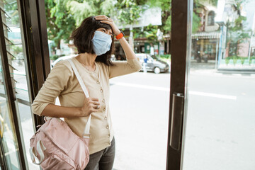 Fototapeta premium Asian woman wearing a mask stands waiting for the bus at the bus stop on a hot day