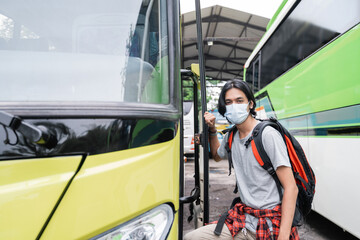 Potrait asian young man wearing face masks getting on the bus.A man wearing a face mask and carrying a backpack gets on the bus at the terminal