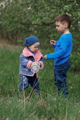 children a boy and a girl in blue clothes play in a blooming spring garden