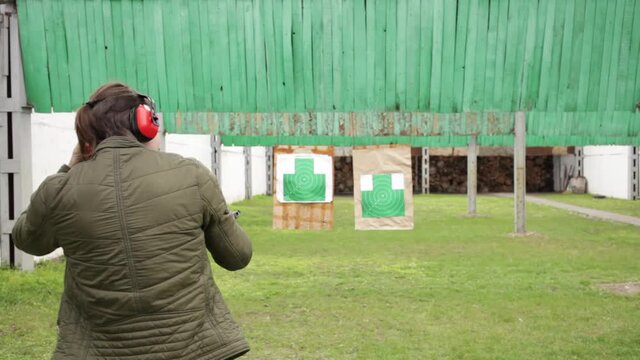 A young man in protective headphones strips from a gun on green targets in the dash. Sports shooting, dangerous firearms, hobbies. outdoors activity back view