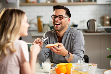 Handsome man enjoying in breakfast with girlfriend. Happy young couple drinking coffee and eating sandwich at home..