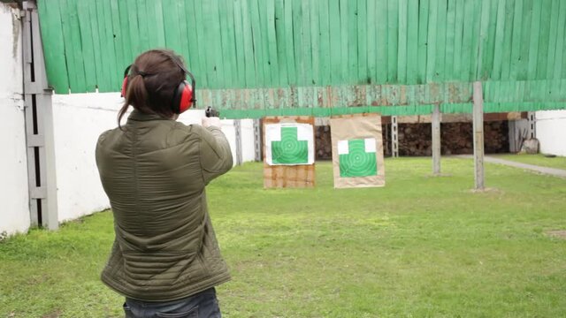 A young man in protective headphones strips from a gun on green targets in the dash. Sports shooting, dangerous firearms, hobbies. outdoors activity green grass