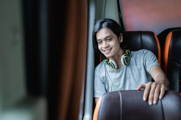 a young man in headphones sits by a window and looks out on a bus ride