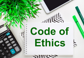 Calculator, green plant, telephone, marker, notebook with the text CODE OF ETHICS on the desktop....