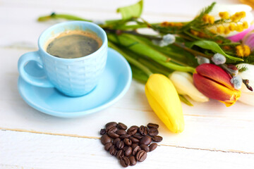 Beautiful bouquet of spring flowers on light wooden background with cup of morning coffee. Background for greetings, invitations , and postcards.