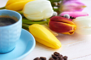 Beautiful bouquet of spring flowers on light wooden background with cup of morning coffee. Background for greetings, invitations , and postcards.