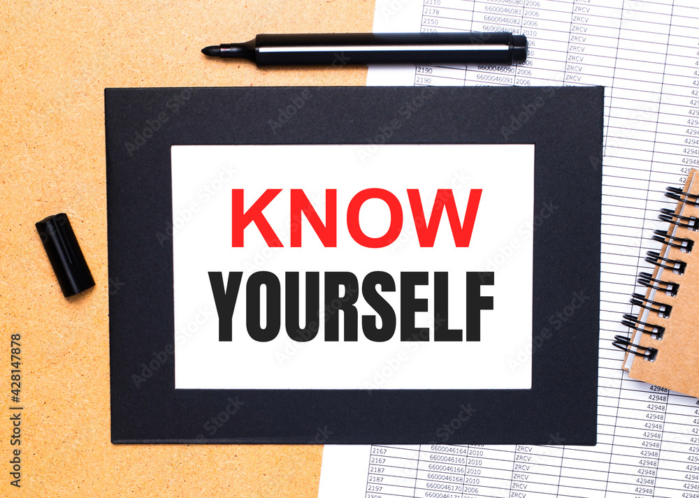 Poster on a wooden table, there is a black open marker, a brown notepad and a sheet of paper in a black fra