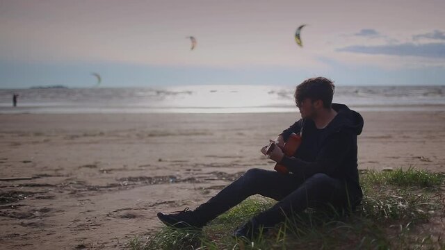 Young man plays the guitar on the seashore.