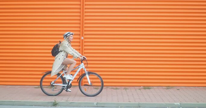 Woman bicyclist in helmet riding on orange background in the city on sport retro bike. 4K video.
