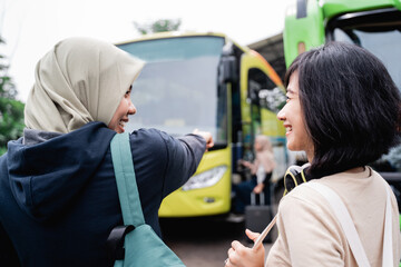 a woman in a headscarf with a finger pointing towards the bus while talking to a woman with headphones while going by bus