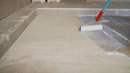 Priming Concrete floor before laying tiles on it, the final preparatory stage for strengthening the surface. Floor priming process.