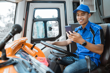 a male driver in uniform looks at his cellphone while holding the wheel in the bus
