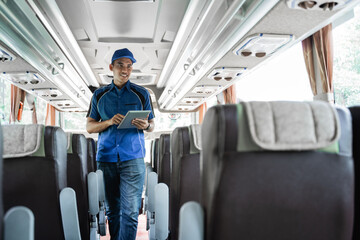 a male bus crew member uses a digital tablet while checking seats on the bus