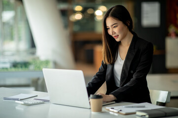 Fototapeta premium Portrait of Businesswoman working on laptop computer doing finances,accounting analysis,report,data and pointing graph at the office.