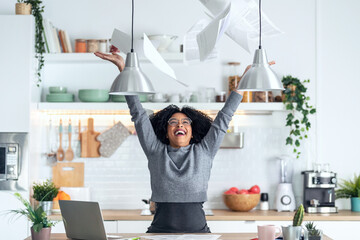 Happy afro business woman tossing invoices and documents into the air while working on the laptop...