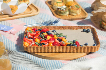 Picnic setting with burgers, tart, croissant, cakes, picnic hamper basket, guitar and food ready for party. Cheerful family sitting on the grass during a picnic in a park. Young smiling family