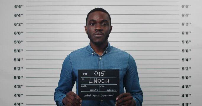 Portrait of afro american male person holding sign for photo in police department. Crop view of young man posing, raising head and looking to camera. Concept of mugshot and crime.