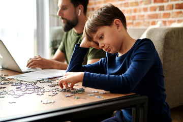 Naklejka premium Boredom boy solving jigsaw puzzle during father working