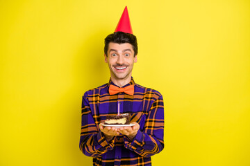 Photo of young excited man happy positive smile wear party hat hold peace of cake birthday isolated over yellow color background